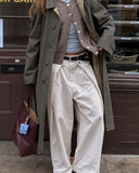 Person wearing a long coat, white pants, and holding a maroon bag with a blue tag.